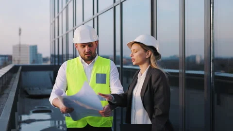 Two construction professionals, a man and a woman, stand on a rooftop discussing Stock Footage 289068539