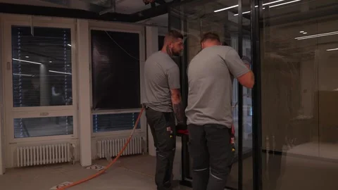 Two construction workers align and fix a large glass partition in a modern Vidéo 331304572