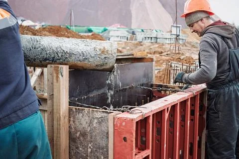Two construction workers are focused on pouring concrete into wooden and meta Stockfoto's