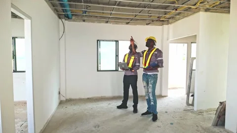 Two construction workers assess ceiling wiring in an unfinished room. Stock Footage 311374871