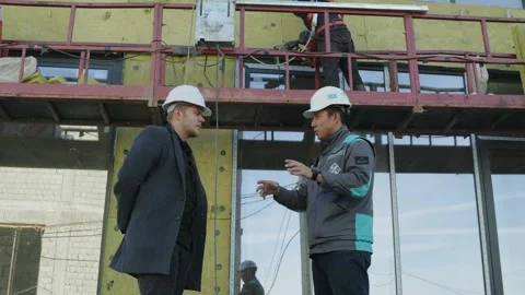 Two construction workers checking plans on a mobile phone on the building site Stock Footage 323174343