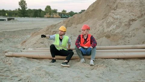 Two construction workers discussing, sitting near sand Fotos de archivo