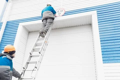 Two construction workers fix sign on automatic garage door for large vehicles. Stock Photos