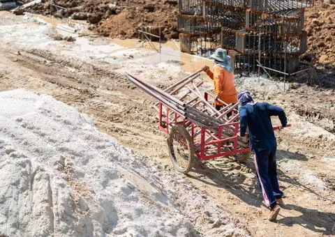 Two construction workers pushing and pulling a heavy red handcart loaded wi.. Stock Photos