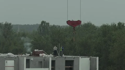 Two construction workers on rooftop of building frame with large crane hook Stock Footage 342922268