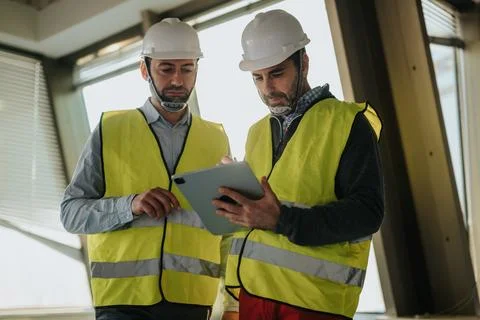 Two construction workers on-site discussing building plans using a digital Foto stock