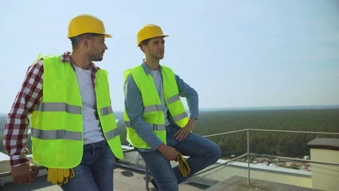 Two construction workers talking during work break on building roof, occupation Video stock 117213004