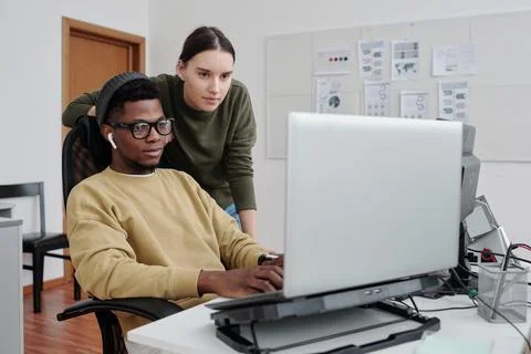 Two contemporary programmers decoding data on laptop screen by workplace Stock Photos