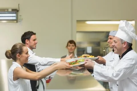Two cooks handing plates to servers Stock Photos