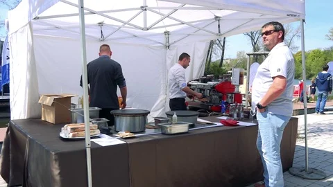 Two cooks prepare meal for a customer under a white tent Video stock 71198638