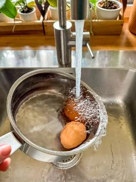 Two Cooling boiled eggs under running water in a stainless pan after cooking Stock Photos