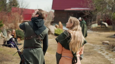 Two costumed figures walking through rustic village yard, rear view with steady Видео 345681456