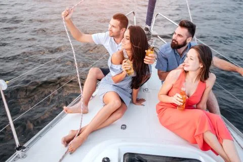Two couples are sitting on bow of yacht. They look to left. Women are excired 스톡 사진