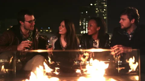 Two couples hanging out on a rooftop bar at night sit in front of a fire pit Video stock 44188896