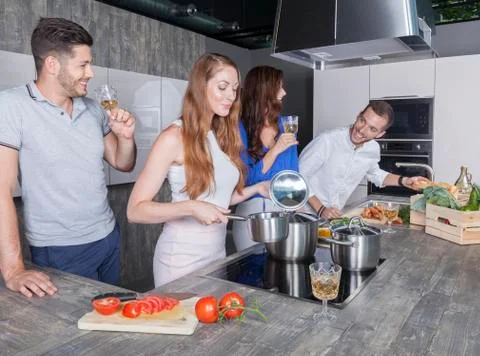 Two couples have fun in the kitchen while cooking and drinking white wine Stock Photos
