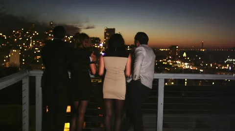 Two couples look over a balcony while hanging out at a rooftop bar at dusk Stock Footage 44117675