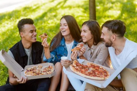 Two couples spending time together, eating pizza in the park Stock Photos
