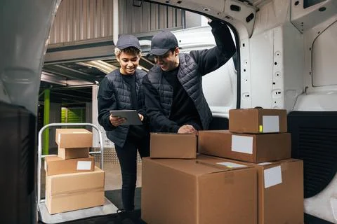 Two couriers in uniform standing at car trunk in warehouse Stock Photos