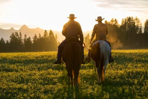 Two cowboys riding on horseback in a Prairie landscape at sunset. Stock Photos