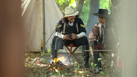 Two cowboys sit at a rustic campsite, sharing a cup of coffee Video stock 326181022