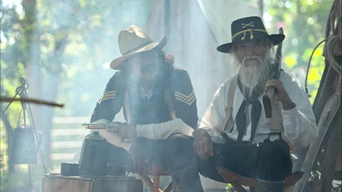 Two cowboys sit at a rustic campsite, sharing a cup of coffee Vídeos de archivo 326210049