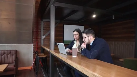 Two coworkers discuss work in a cafe with a laptop and coffee sitting at the Stock-Footage 85403225