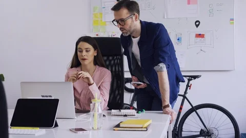 Two coworkers discussing while looking at laptop in small office Stock Footage 102859650