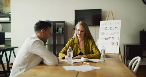 Two coworkers go over notes at meeting at wood desk in modern office during the Stock Footage 199457976