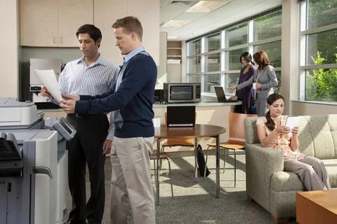 Two coworkers talking at printer while in breakroom at office. Foto stock