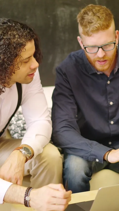 Two coworkers talking while using laptop sitting on a sofa Stock Footage 260849779