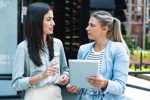 Two coworkers using a digital tablet and talking while standing outside. Mo.. Stock Photos