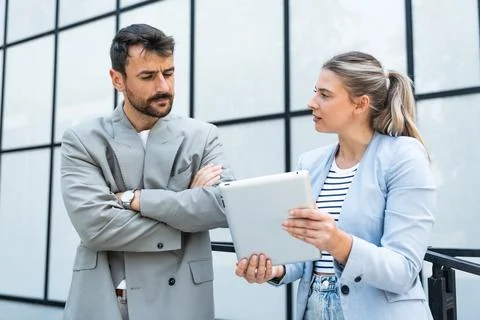 Two coworkers using a digital tablet and talking while standing outside. Mo.. Stock Photos