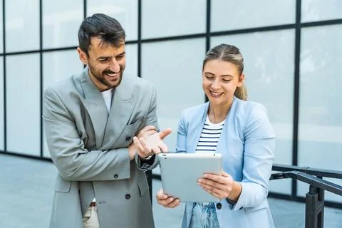 Two coworkers using a digital tablet and talking while standing outside. Mo.. Stock Photos