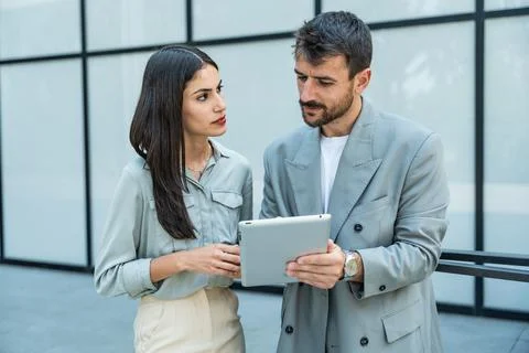 Two coworkers using a digital tablet and talking while standing outside. Mo.. Stock Photos