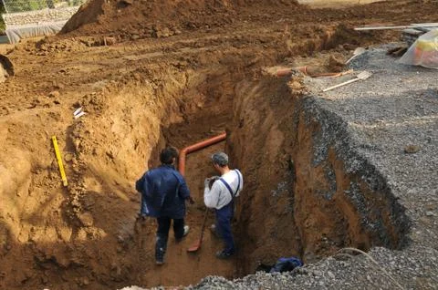 Two craftsmen in a construction pit working on a pipe control system Stock Photos