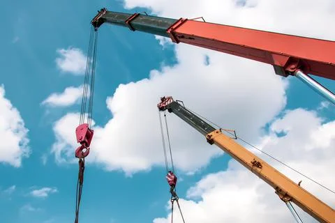 Two crane arrows with hooks on the background of the sky and clouds Stock Photos