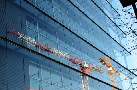 Two cranes are reflected in a glass wall of building Stock Photos