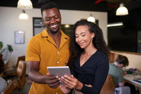 Two creative colleagues look at a digital tablet in an open plan office Stock Photos