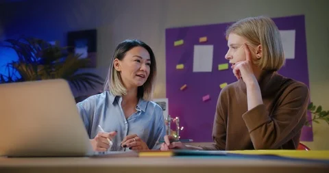 Two creative mixed race female communicating sitting behind desk in cozy Stock Footage 123673397