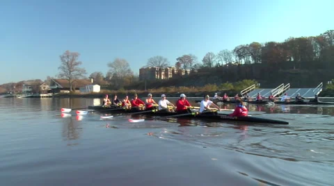 Two crew boats row up river near shore Stock Footage 998247