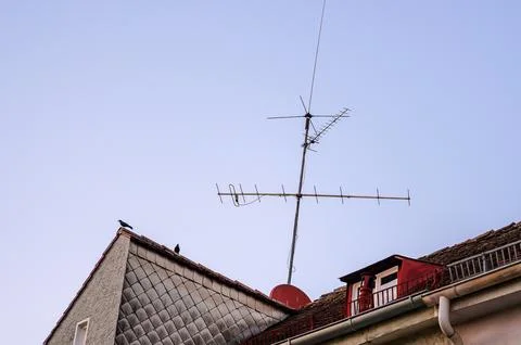 Two crows perched on a rooftop with an old television antenna against a cle.. 스톡 사진