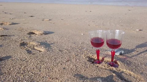 Two crystal glasses with red wine on sandy beach. Large sea waves, white foam Stock Footage 144111285
