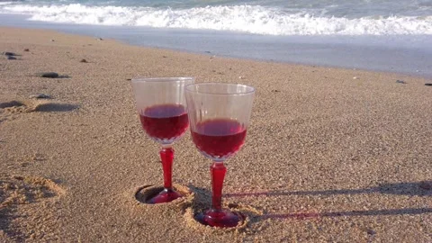 Two crystal glasses with red wine on sandy beach. Large sea waves, white foam Stock Footage 144111300