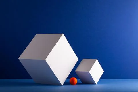 Two cubes with orange golf ball on the blue background. 스톡 사진