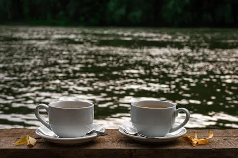 Two cup of hot coffee is placed on a wooden table with a river Stock Photos