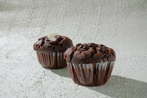 Two of cupcakes on textured white: one chocolate with chocochips and one ch.. Stock Photos