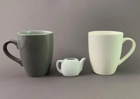 Two cups and a small kettle on a gray background. Dark and light mug for tea  Stock Photos