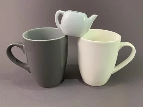 Two cups and a small kettle on a gray background. Dark and light mug for tea  Stock Photos