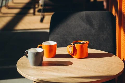 Two cups and a teapot on a table in a cafe with hard shadows. Stock Photos