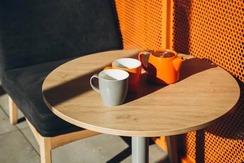 Two cups and a teapot on a table in a cafe with hard shadows. Stock Photos